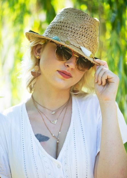 A person wearing a wide-brimmed hat and sunglasses, standing in a sunny outdoor setting, emphasizing sun protection through accessories.
