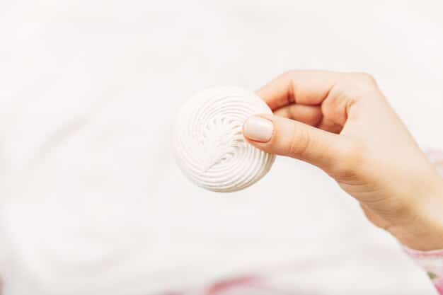 A close-up shot of a woman's hand applying toner to a cotton pad, with a bottle of toner and other skincare products blurred in the background. Focus on the texture of the cotton pad and the clarity of the toner solution.