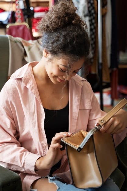 A woman is carefully examining a vintage handbag in a consignment shop, checking the stitching, hardware, and overall condition. She is holding a magnifying glass and appears to be very thorough in her inspection. The background is slightly blurred to focus on her detailed examination.