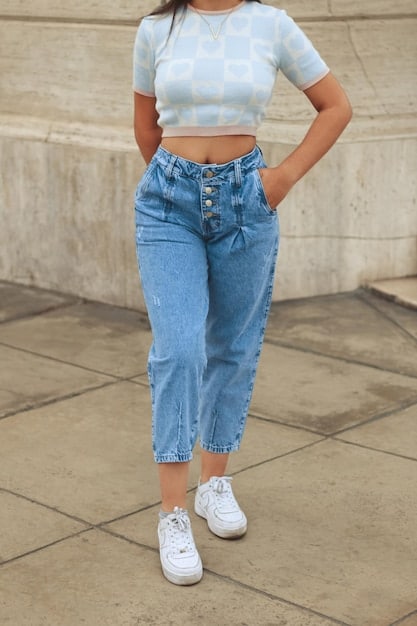 A close-up of a woman's lower body showcasing wide-leg denim pants paired with white sneakers. The focus is on the fit and style of the pants and how they complement the footwear for a casual look.