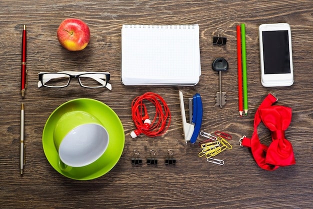 A collection of essential accessories arranged on a wooden surface. The accessories include a classic scarf, a leather belt, simple jewelry pieces (necklace and earrings), and a pair of neutral-colored shoes.