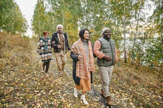 A diverse group of people walking in a park during autumn, each wearing a different layered outfit that showcases warm colors like burgundy, mustard yellow, and olive green. The focus is on the variety of textures and styles.