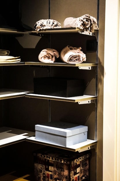 A close-up shot of a neatly organized closet featuring several key elevated basic items: a crisp white button-down shirt, a cashmere sweater, dark wash jeans, and a tailored blazer. The image focuses on the texture and quality of the fabrics.