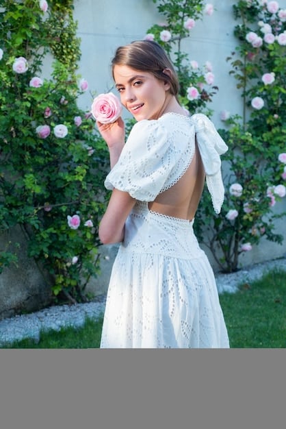 A woman wearing a blush-colored lace dress with delicate floral embroidery, standing in a garden with soft, natural light.