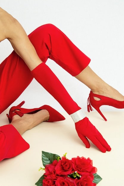 A woman showcasing her statement shoes - a pair of vibrant red ankle boots with a metallic heel. She is wearing simple jeans and a black top, allowing the shoes to stand out and add a pop of color to her outfit.