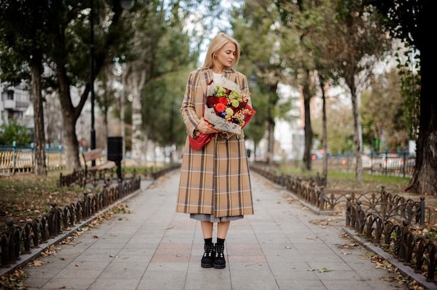 A woman in a park wearing a black blazer, a rust-colored midi skirt, and brown ankle boots. She is holding a beige tote bag and smiling, capturing the essence of a chic and practical transitional outfit. The backdrop features trees with autumn leaves, reinforcing the seasonal change.