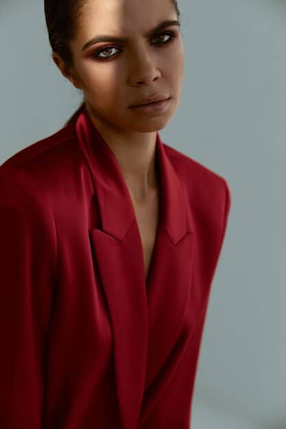 A close-up shot of a woman wearing a monochromatic power suit in a deep burgundy color, showcasing the different textures of the velvet blazer and silk trousers, accessorized with a delicate gold necklace.