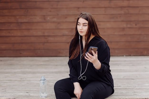 A close-up shot of a woman wearing high-waisted black leggings and a gray oversized hoodie. She is sitting on a park bench, holding a phone, and smiling