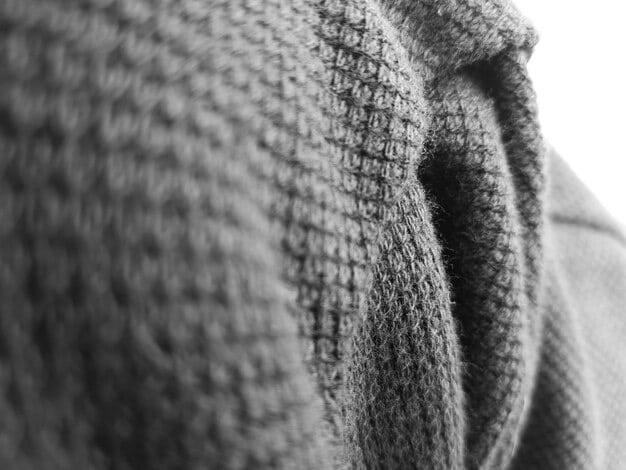 A close-up shot of various textures in a monochrome outfit. Featured are a ribbed knit sweater, smooth leather belt, and textured wool pants, all in varying shades of gray. The image highlights the subtle differences in material that add depth to a single-color ensemble.